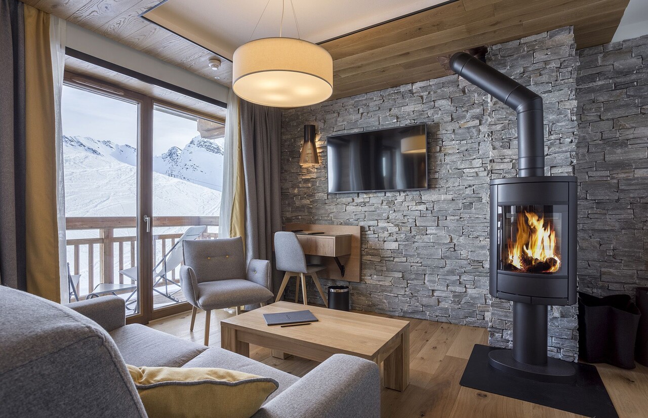 Mur en parement de pierre naturelle dans un chalet, avec poêle à bois et vue sur les montagnes